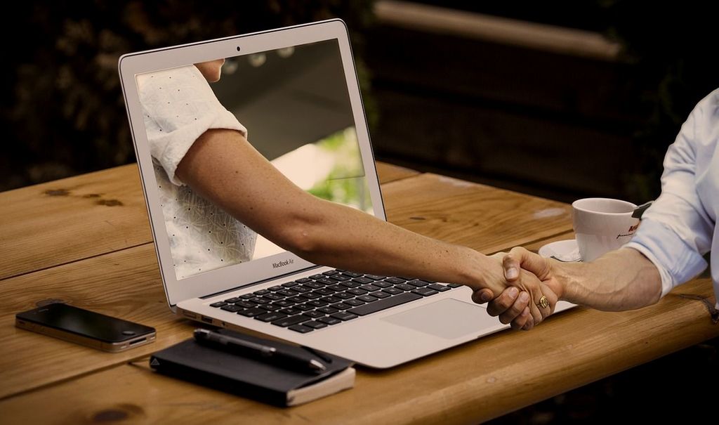 Stretta di mano attraverso lo schermo di un laptop – counseling online in videochiamata
